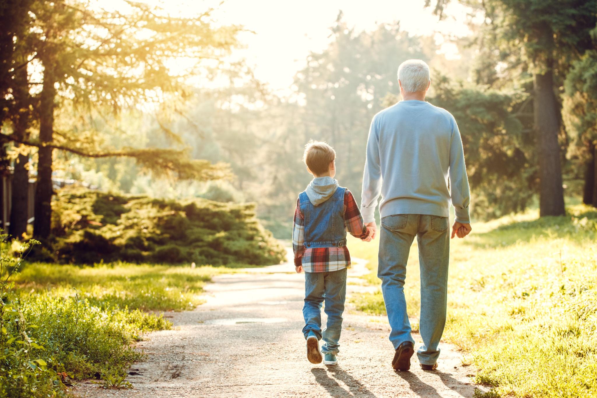 A man and a little girl walking down a tree lined road.